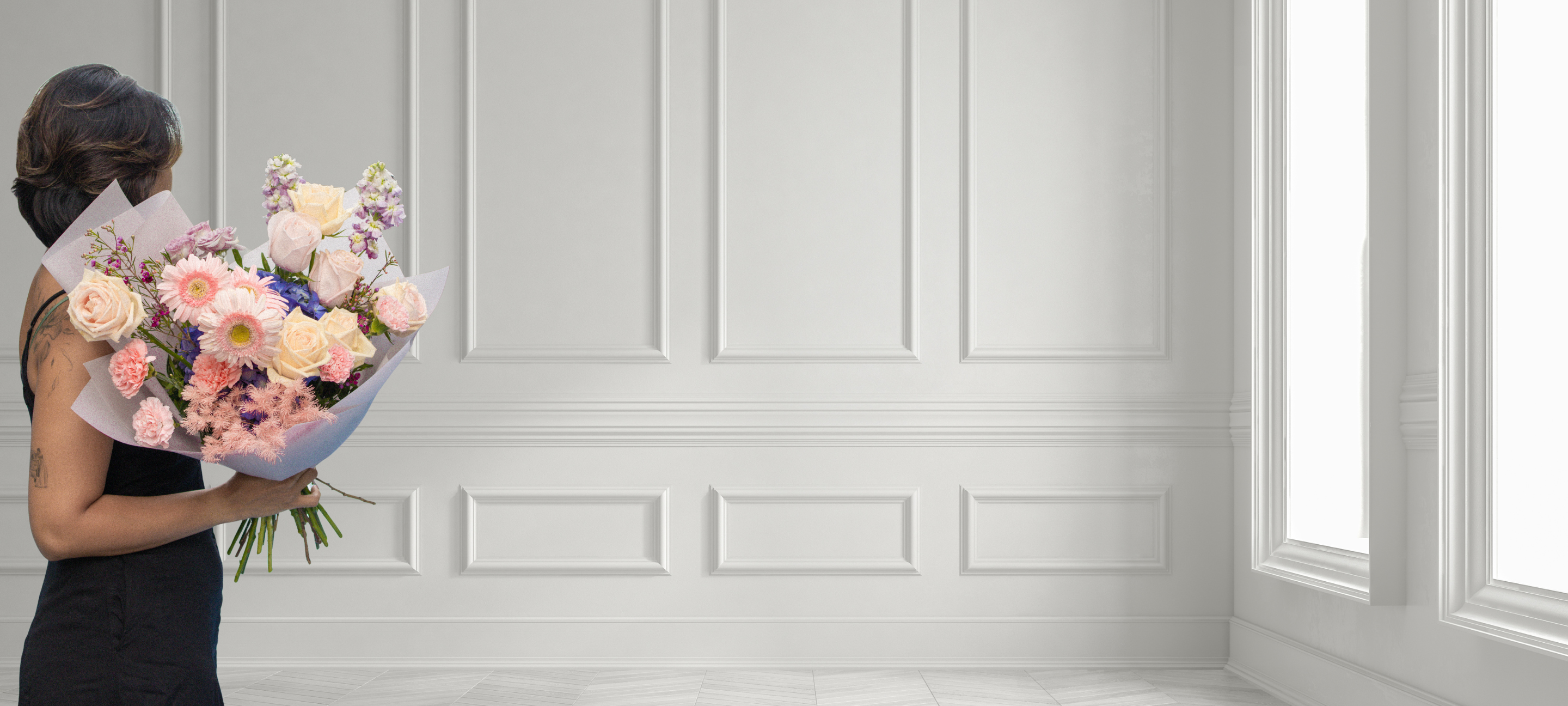 Woman holding a bouquet of flowers in a minimalistic room with white paneled walls and a window.